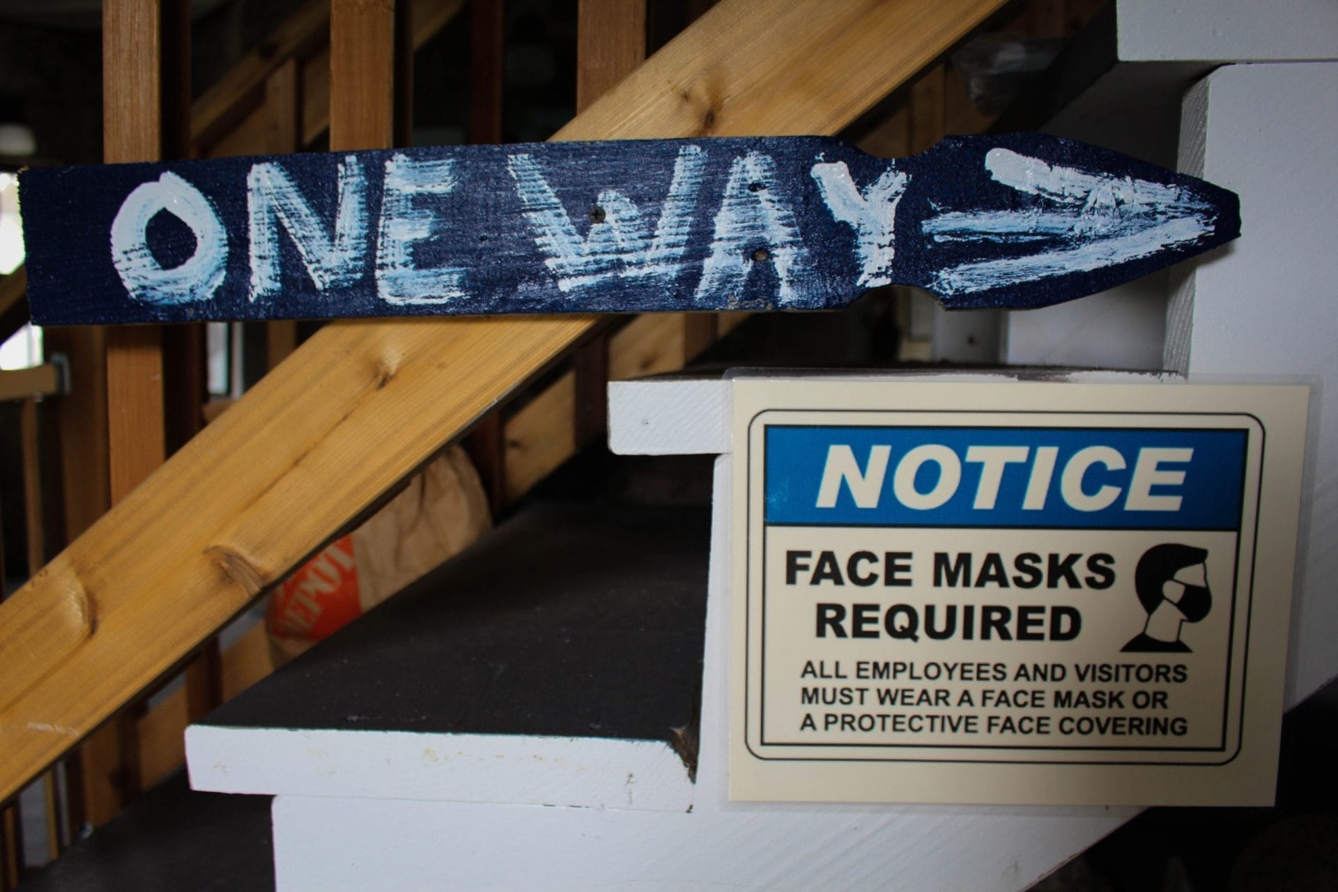 A staircase with a One Way sign painted on a wooden arrow leads to an area reminiscent of Bannerman Castle. Next to it, a Notice sign indicates that face masks are required for all employees and visitors, with an image of a face mask.