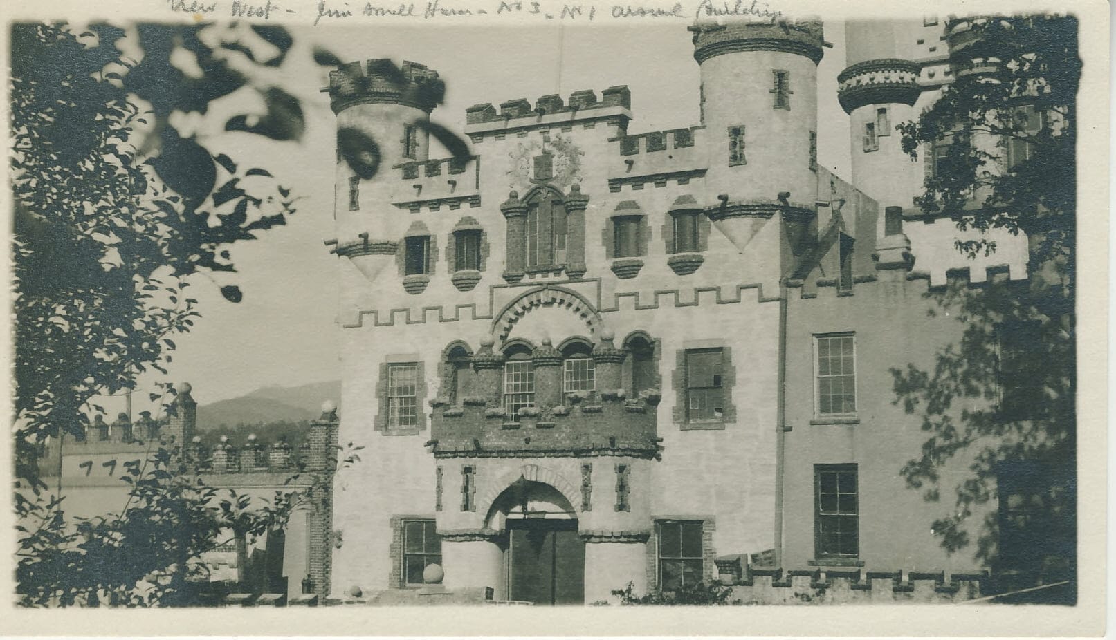 Bannerman Castle stands with its historic turrets and battlements, partially obscured by branches in the foreground. The building, rich with ornate architectural details, is set against a clear sky.