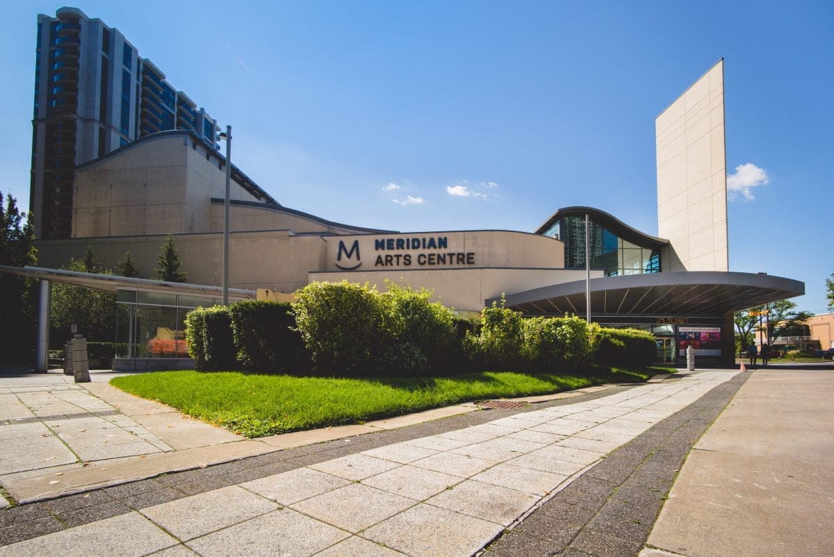 Wide-angle view of the Meridian Arts Centre, a modern building with a unique architectural design, surrounded by lush greenery. The clear blue sky provides a stunning backdrop to the Meridian Arts Centers contemporary charm.