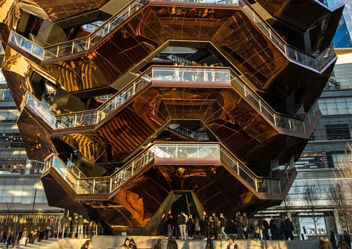 Exterior view of a large, honeycomb-like structure with people on staircases connecting various levels. Bathed in the suns warm glow, its metallic surface gleams like golden leaves in fall. Nestled in an urban area near an Amtrak station, city buildings rise majestically in the background. Exterior view of a large, honeycomb-like structure with people on staircases connecting various levels. Bathed in the suns warm glow, its metallic surface gleams like golden leaves in fall. Nestled in an urban area near an Amtrak station, city buildings rise majestically in the background.