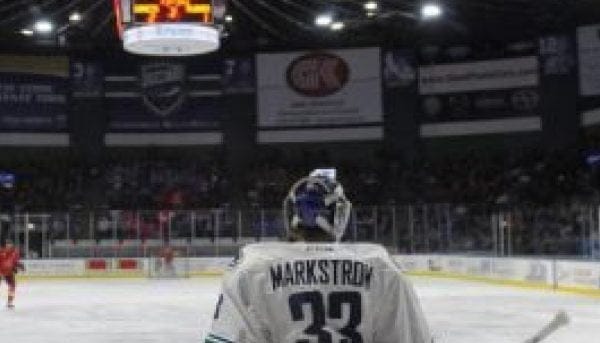 A hockey goalie in a jersey with Markstrom and number 33 stands on the ice rink in Central New York. The scoreboard reads 7:34, while the packed stands buzz with eager spectators.