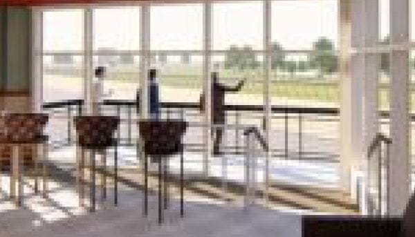 A bright room with tall windows offers a scenic view of Saratoga Springs outside. Three people stand near the windows, with two high chairs and a table in the foreground, suggesting a modern, casual gathering space.
