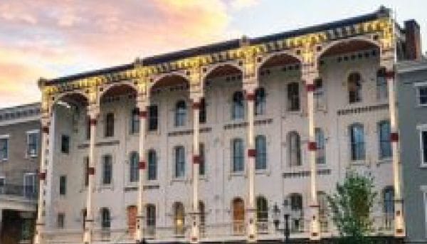 Under a colorful sunset sky, a historic Saratoga Springs building boasts ornate columns and arches. This architectural gem features detailed elements and a row of windows spanning three floors, capturing the essence of past elegance.