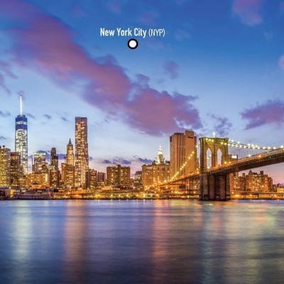 The skyline of New York City at dusk reveals illuminated skyscrapers standing tall over tranquil waters, with the iconic Brooklyn Bridge in view. The label New York City (NYP) crowns this breathtaking scene.