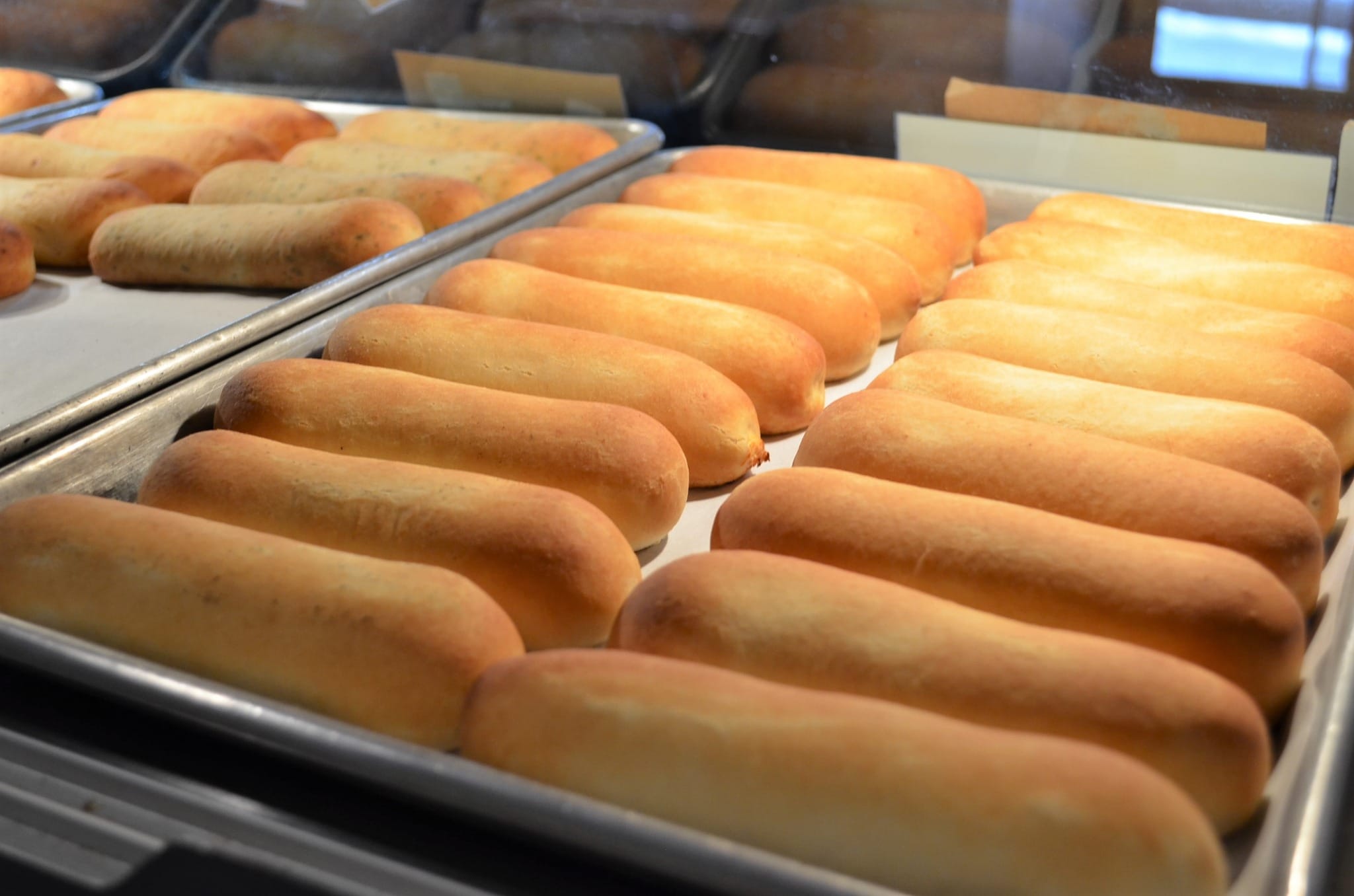Rows of golden-brown breadsticks are lined up neatly on metal baking trays behind a glass display case, offering visitors a true taste of New York regional dishes perfect for any Empire State Eats adventure.