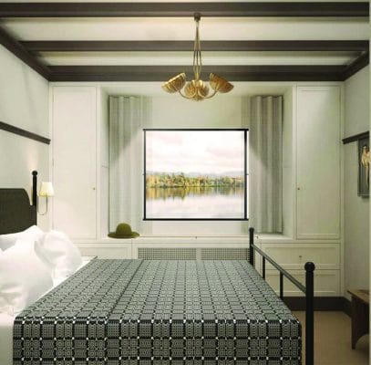 A cozy bedroom with a patterned bedspread, white walls, a large window showing a scenic lake view, built-in cabinets, and a modern ceiling light fixture. A hat rests on the window seat.