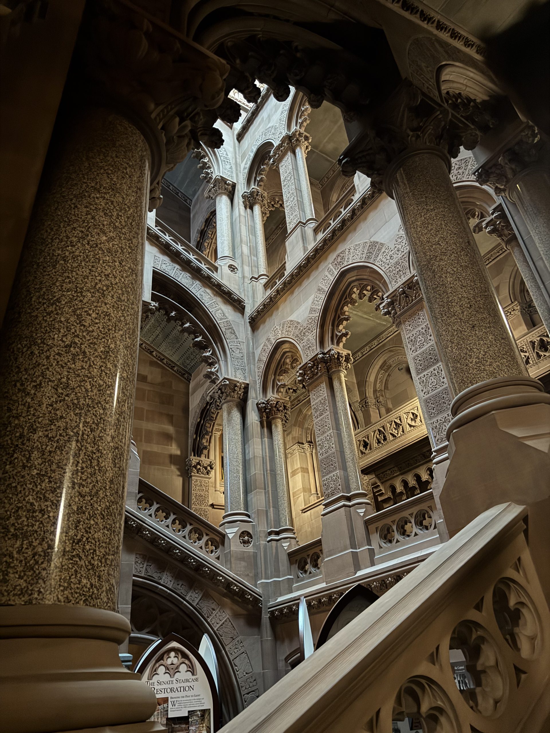 Grand stone columns and arches in an ornate, historic building with intricate carvings and dramatic lighting, viewed from a staircase—an atmosphere that evokes the lingering mystery of The One That Got Away.